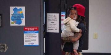 Una mujer sostiene a su bebé mientras vota en una cabina