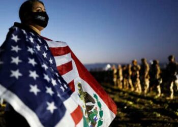 Un manifestante agita una bandera estadounidense-mexicana cerca de los miembros de la Guardia Nacional y los agentes federales que bloquean a los manifestantes durante una redada de inmigración de hielo en una granja de cannabis con licencia cercana el 10 de julio de 2025, cerca de Camarillo, California.