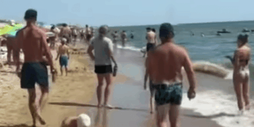 Playa llena de gente con gente caminando sobre la arena y en el agua.