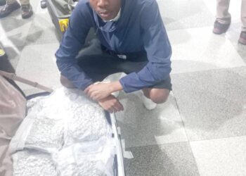 Un joven se arrodilla junto a una maleta llena de cannabis.