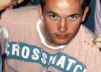 Foto de primer plano de un joven con cabello puntiagudo con una camisa rosa con un diseño azul.