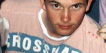 Foto de primer plano de un joven con cabello puntiagudo con una camisa rosa con un diseño azul.