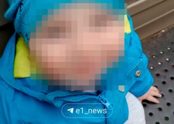 Foto de un niño pequeño con la cara borrosa, con una chaqueta y un sombrero azules.