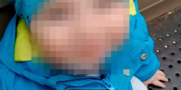 Foto de un niño pequeño con la cara borrosa, con una chaqueta y un sombrero azules.