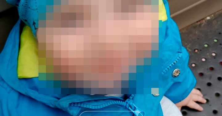 Foto de un niño pequeño con la cara borrosa, con una chaqueta y un sombrero azules.