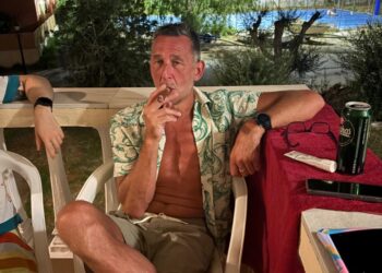 Hombre fumando un cigarro en un patio por la noche.