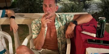 Hombre fumando un cigarro en un patio por la noche.