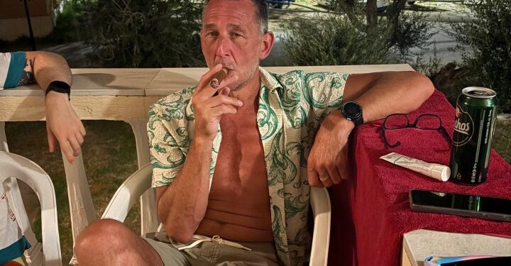 Hombre fumando un cigarro en un patio por la noche.