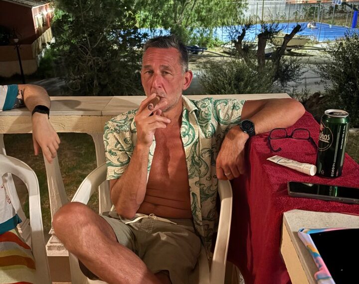 Hombre fumando un cigarro en un patio por la noche.