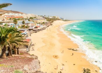 Playa de arena en Morro Jable, Fuerteventura con agua turquesa y hoteles.