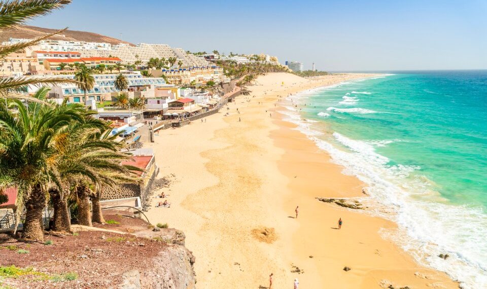 Playa de arena en Morro Jable, Fuerteventura con agua turquesa y hoteles.
