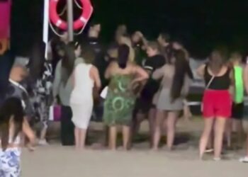 La multitud se reunió en una playa por la noche cerca de un salvavidas.