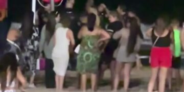 La multitud se reunió en una playa por la noche cerca de un salvavidas.