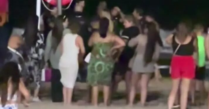La multitud se reunió en una playa por la noche cerca de un salvavidas.