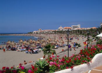 Escena de playa con gente relajada en sillones bajo paraguas.