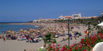 Escena de playa con gente relajada en sillones bajo paraguas.