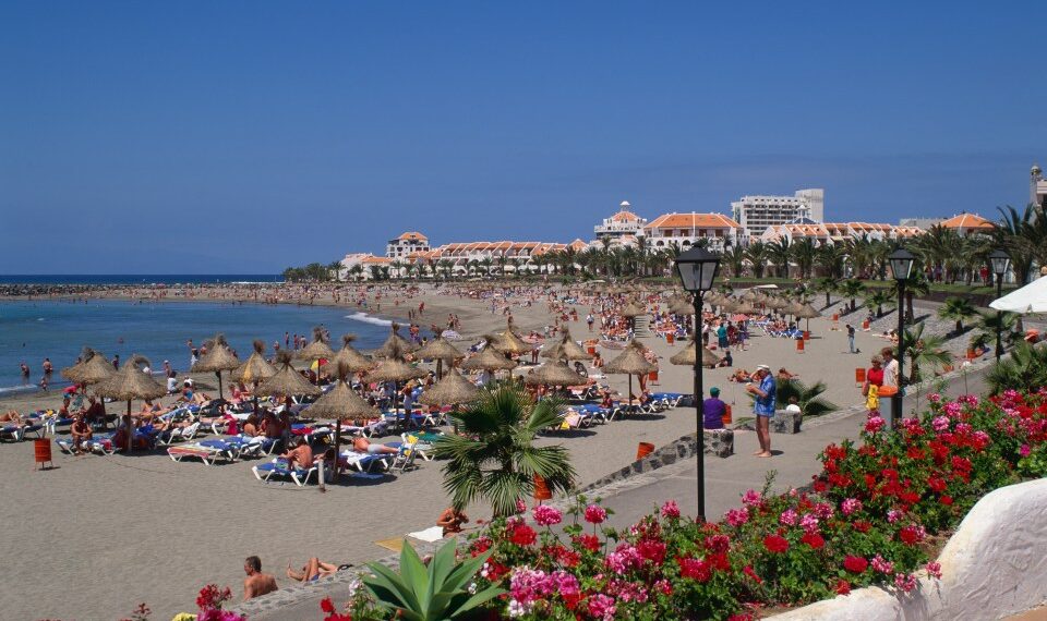 Escena de playa con gente relajada en sillones bajo paraguas.