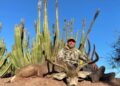 Cazador posando con un gran ciervo de mula del desierto.