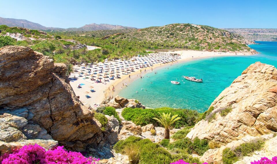 Vai Beach en Creta, Grecia: palmeras, agua turquesa y gente que se relaja en la costa arenosa.