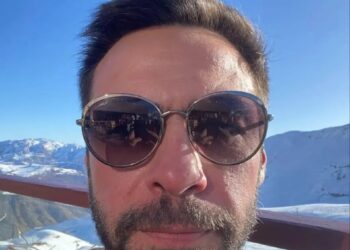 Selfie de un hombre con gafas de sol, con montañas nevadas en el fondo.