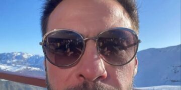 Selfie de un hombre con gafas de sol, con montañas nevadas en el fondo.