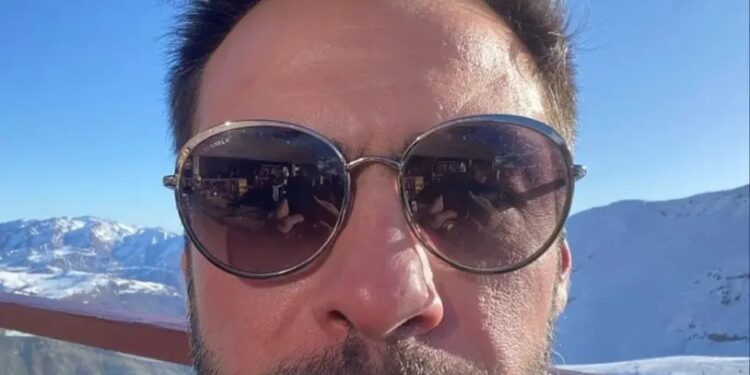 Selfie de un hombre con gafas de sol, con montañas nevadas en el fondo.