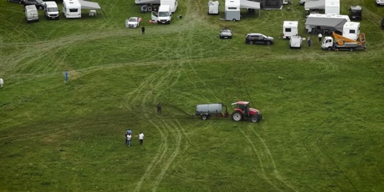 Vista aérea de un tractor que extiende el estiércol en un campo con varias caravanas estacionadas cerca.