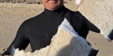 Surfer sosteniendo una tabla de surf dañada por el tiburón.