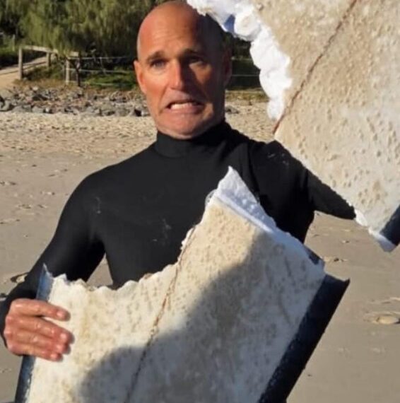 Surfer sosteniendo una tabla de surf dañada por el tiburón.