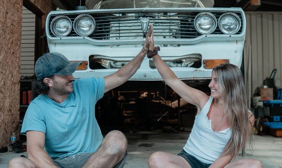 Pareja dando un alto cinco frente a un automóvil.