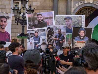 Un portavoz de los medios de comunicación en Barcelona habla en una conferencia de prensa con personas con retratos de los periodistas de Al Jazeera recientemente asesinados en Gaza por el ejército israelí.