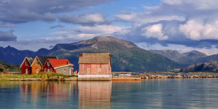 Coloridas cabañas de madera en la isla de Sommaroy, Noruega, con montañas en el fondo.