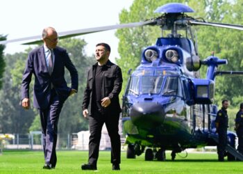 Volodymyr Zelensky y Friedrich Merz caminando en un jardín, con un helicóptero en el fondo.