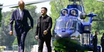 Volodymyr Zelensky y Friedrich Merz caminando en un jardín, con un helicóptero en el fondo.