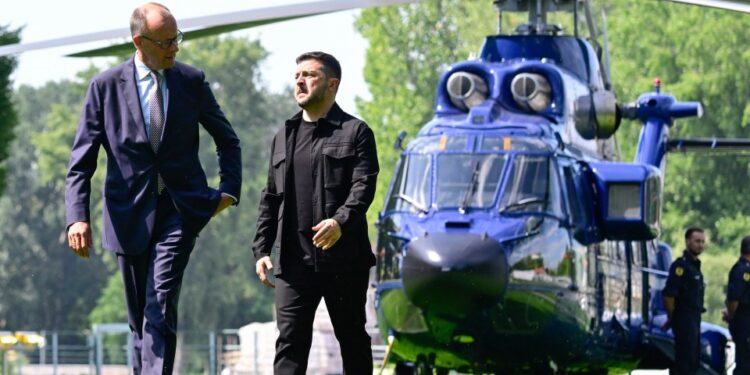 Volodymyr Zelensky y Friedrich Merz caminando en un jardín, con un helicóptero en el fondo.