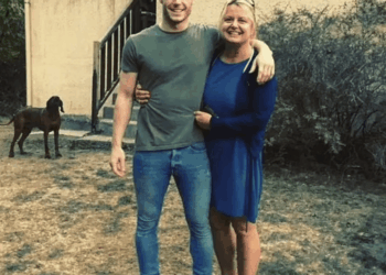 Hombre y mujer que abrazan al aire libre con un perro en el fondo.