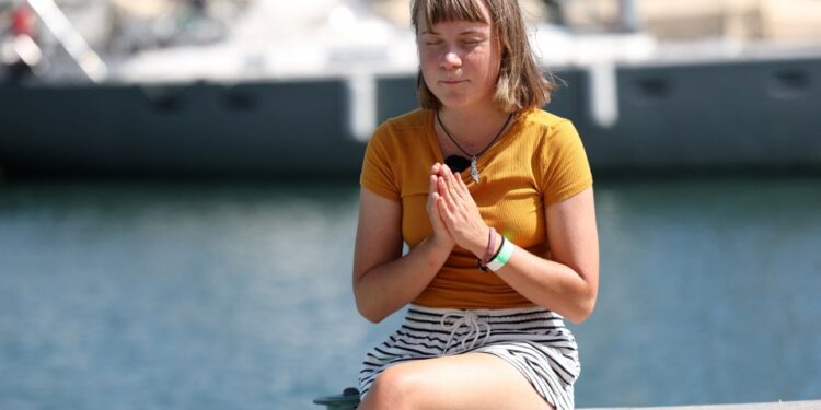 Greta Thunberg se sienta en un bote, con los ojos cerrados, las manos juntas.