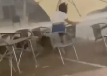 Una camarera lucha por aferrarse a un paraguas de patio durante una fuerte tormenta de viento.