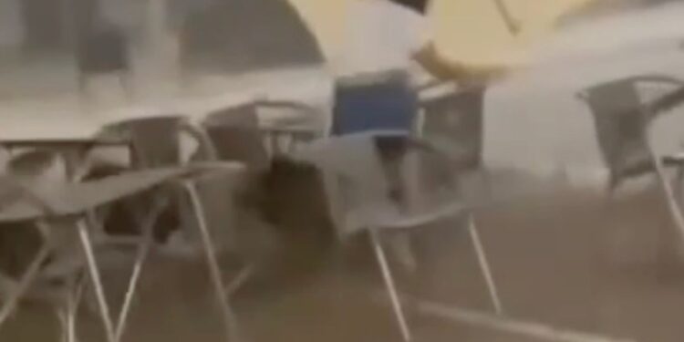 Una camarera lucha por aferrarse a un paraguas de patio durante una fuerte tormenta de viento.