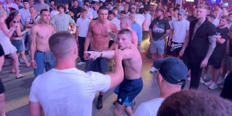 Hombres peleando en una calle llena de gente.