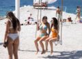 Dos mujeres en bikinis están sentadas en un columpio en la playa.