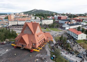 Vista aérea de una iglesia que se traslada a un sistema de transporte, con mucha gente observando.