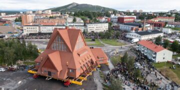 Vista aérea de una iglesia que se traslada a un sistema de transporte, con mucha gente observando.