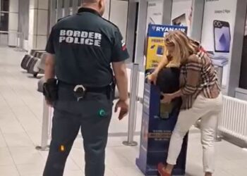 Una mujer lucha por encajar su bolso en un Sizer de equipaje de Ryanair mientras un oficial de policía fronteriza observa.