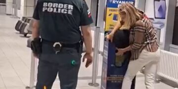 Una mujer lucha por encajar su bolso en un Sizer de equipaje de Ryanair mientras un oficial de policía fronteriza observa.