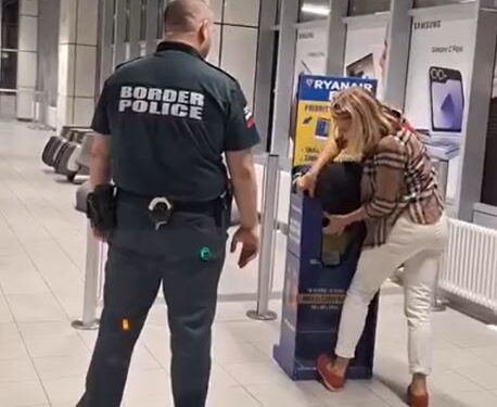 Una mujer lucha por encajar su bolso en un Sizer de equipaje de Ryanair mientras un oficial de policía fronteriza observa.