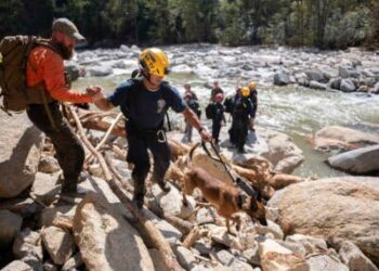 Un miembro del equipo de búsqueda y rescate civil, a la izquierda, da una mano a un miembro de un equipo de búsqueda y rescate urbano de FEMA mientras caminan por el río Broad después del huracán Helene el 2 de octubre de 2024 cerca de Chimney Rock, Carolina del Norte.