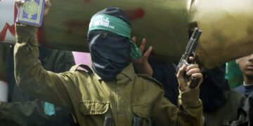 Enmascarado al militante de Hamas sosteniendo una pistola y un Corán durante una manifestación de Cisjordania.