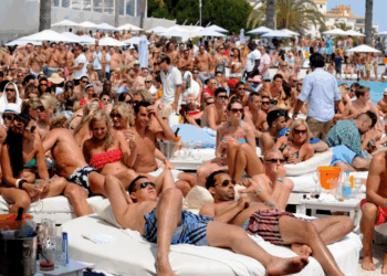 Escena de clubes de playa llenos de gente con gente descansando en camas de día blancas.