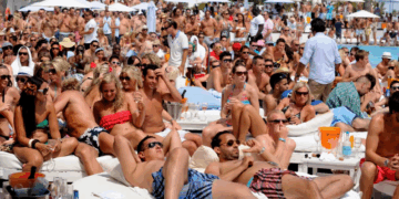 Escena de clubes de playa llenos de gente con gente descansando en camas de día blancas.
